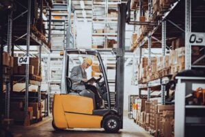 A man in warehouse on a forklift moving between tall storage racks in San Francisco & Sacramento
